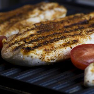 Close-up of grilled chicken breasts with tomatoes sizzling on a barbecue grill, perfect for a delicious meal.