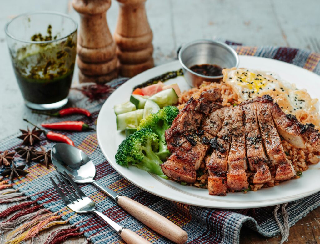 Delicious grilled pork with broccoli, cucumber, and egg served on rice for a tasty meal.